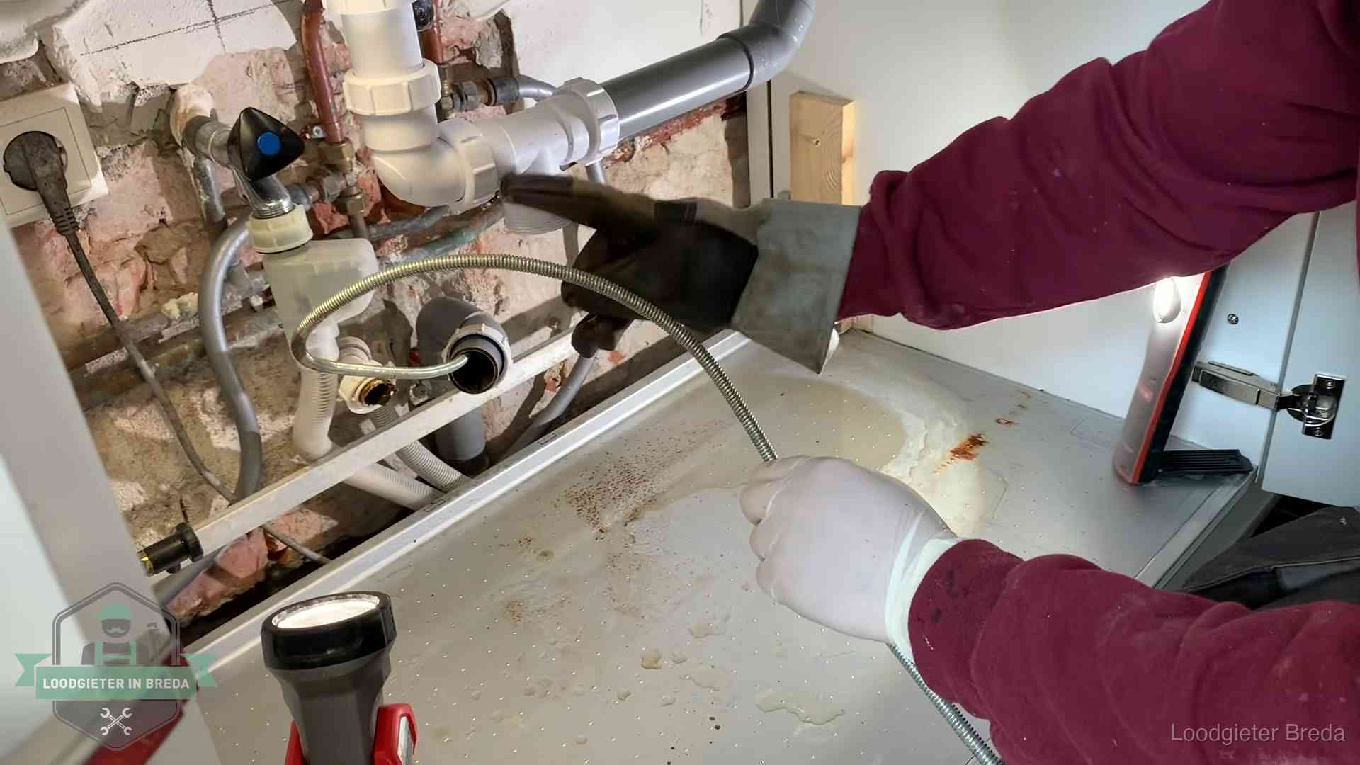 Ontstoppingsveer gaat in een geopende sifonaansluiting onder het aanrecht in Breda