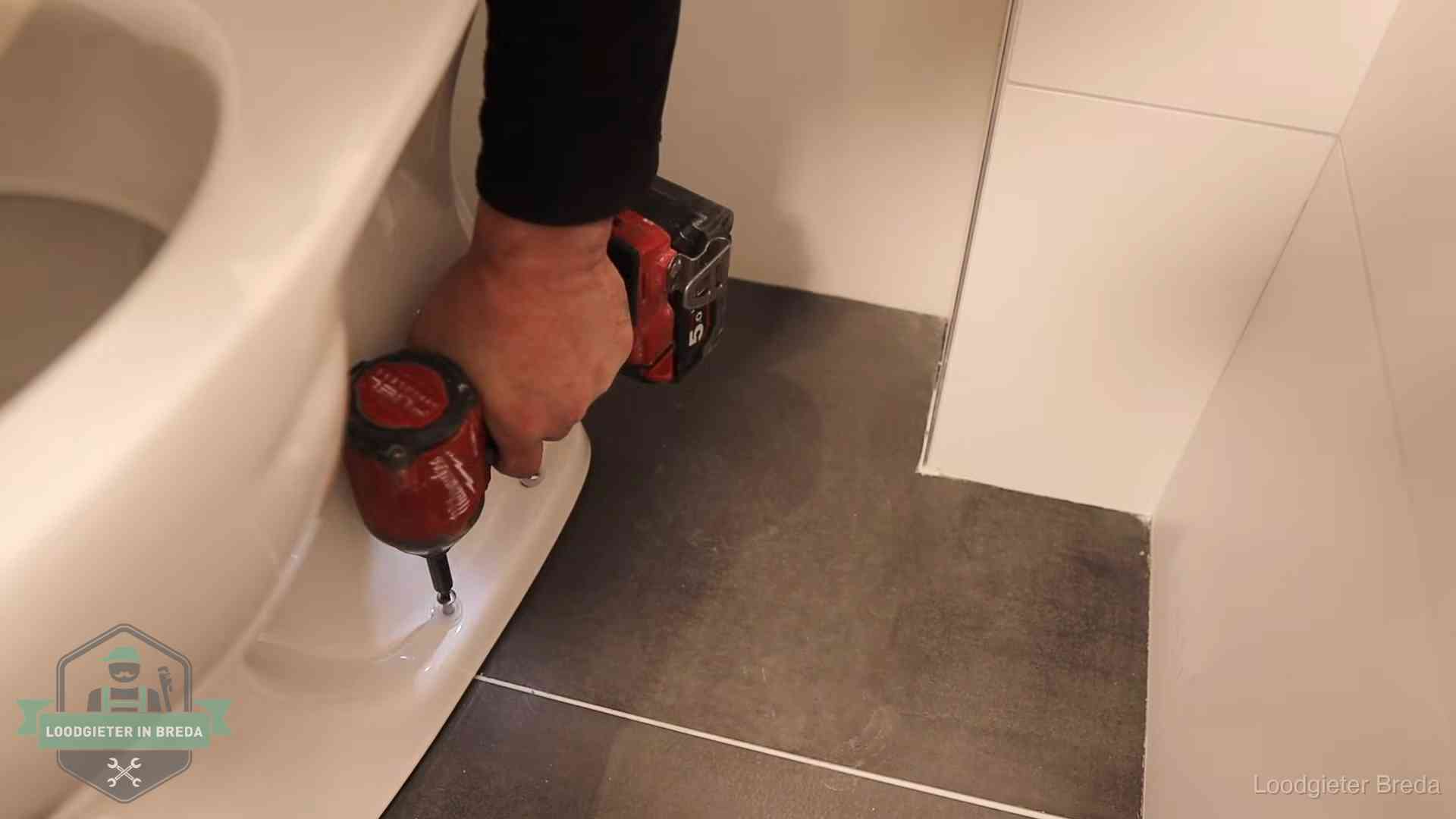 Loodgieter zet de voet van een wc-pot vast op de tegelvloer in Breda